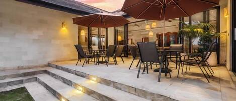 An outdoor patio with a dining set, umbrellas, and steps leading to a building.