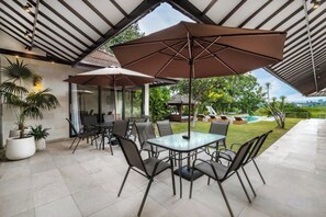 Un patio al aire libre con mesa y sillas, grandes sombrillas y plantas en macetas.