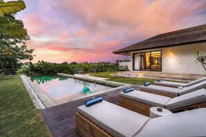 Un espace piscine extérieur moderne, avec des chaises longues et une maison en arrière-plan.