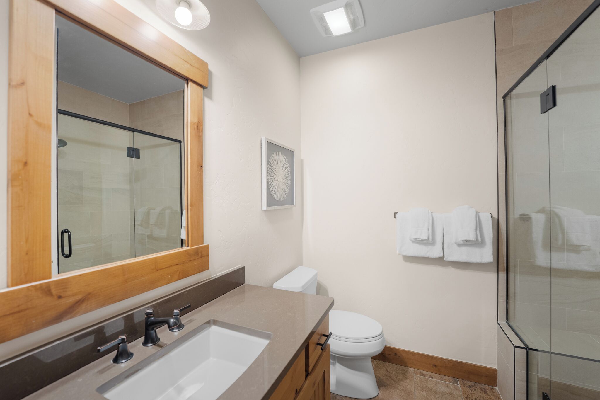 Un bany modern amb un mirall gran, un lavabo, un vàter i una cabina de dutxa de vidre.