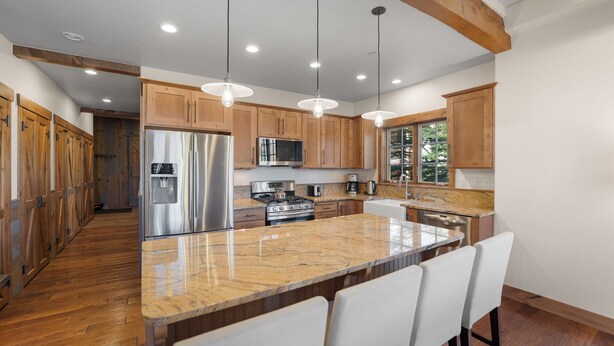 A modern kitchen with wooden cabinets, stainless steel appliances, and a marble island with bar seating. - Wm102cf-2 (Frisco)