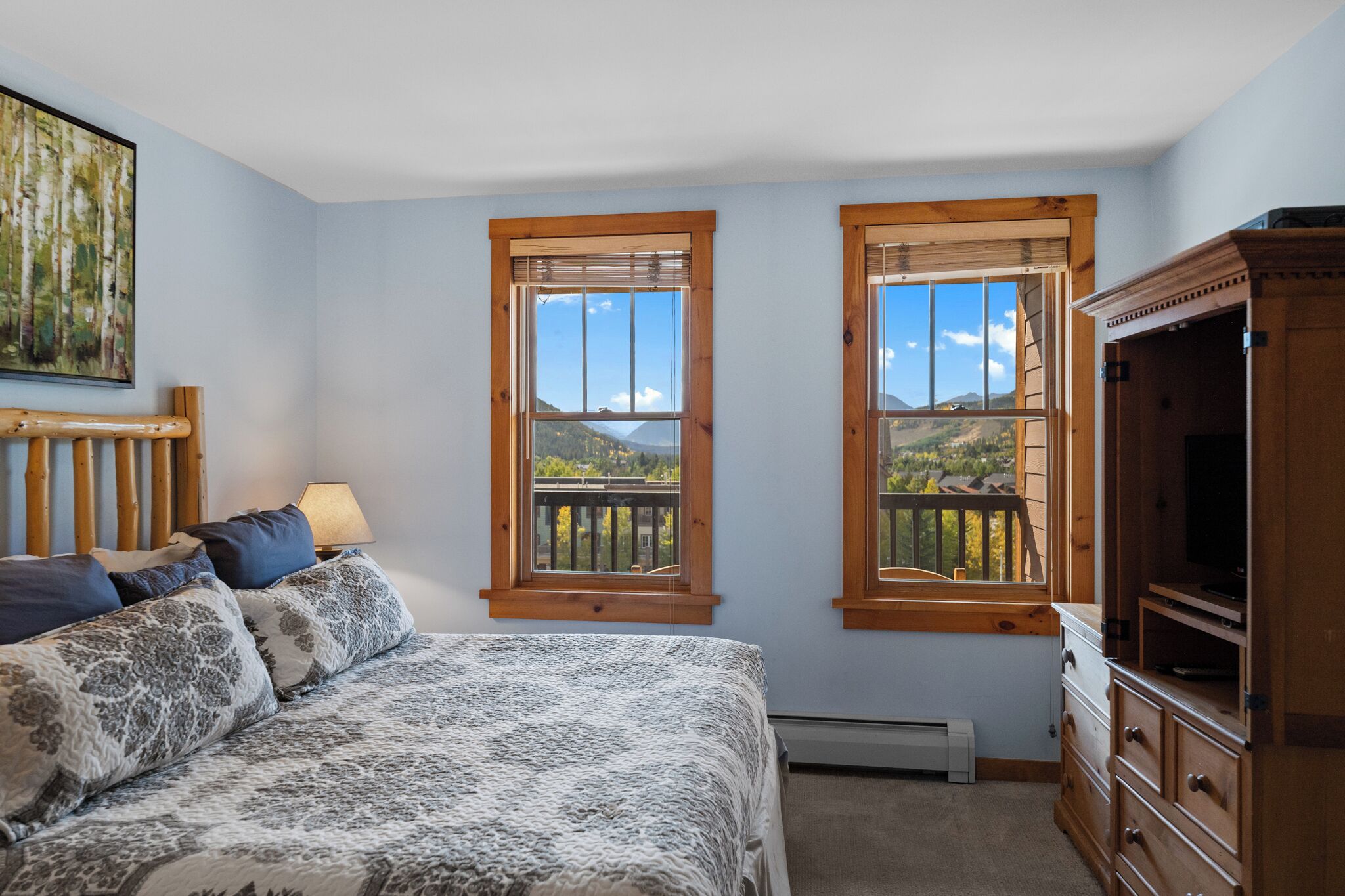 Un dormitorio con una cama, dos ventanas de madera, un aparador y un cuadro en la pared.