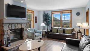 A living room with a stone fireplace, a flat-screen TV, a sofa, a coffee table, and a view of the outdoors. - Bl8392-2 (Keystone)