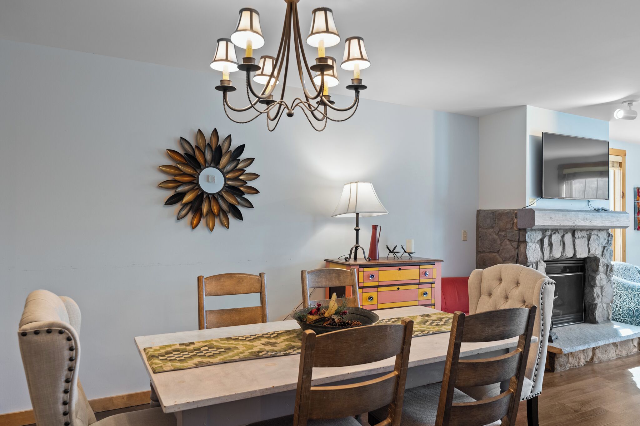 Un comedor con candelabro, un adorno de pared, un televisor y una chimenea de piedra.