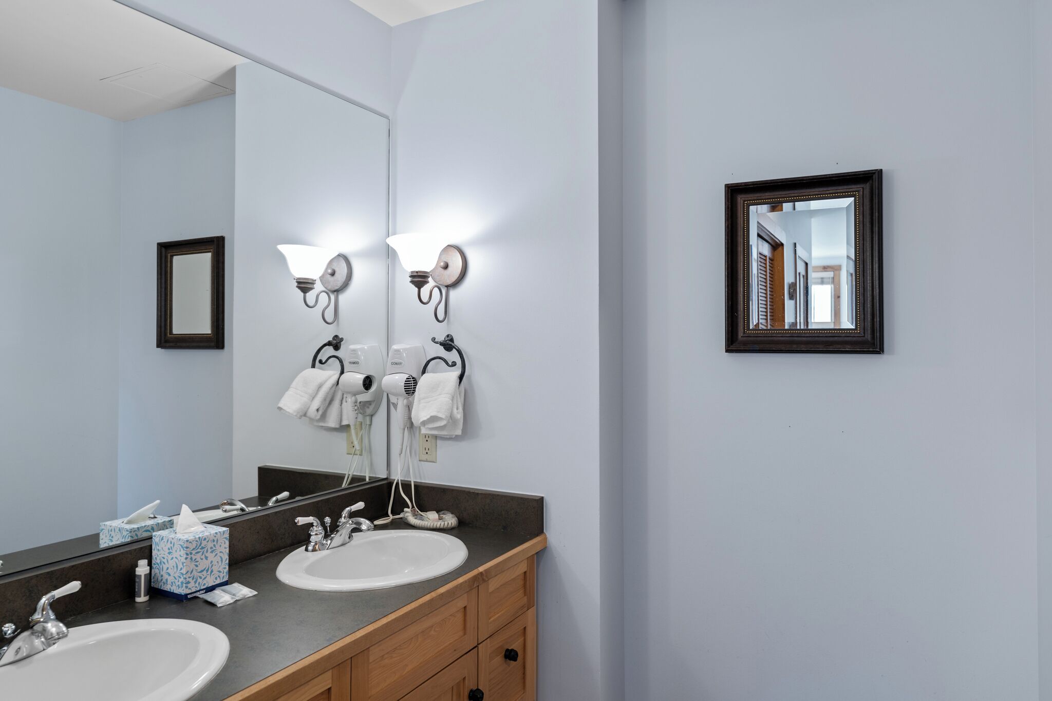 A bathroom with two sinks, a large mirror, and wall-mounted hair dryers.