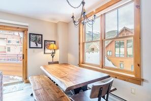 A dining area with a wooden table and benches, large windows with a view of buildings and mountains, and a chandelier.