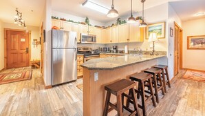 Una cocina con armarios de madera, electrodomésticos de acero inoxidable, encimera de granito y taburetes de bar.