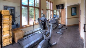 Uma academia com esteiras, bicicletas ergométricas e uma televisão presa à parede.