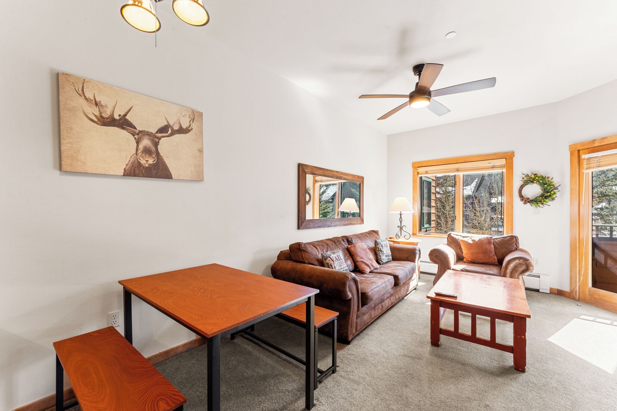 A living room with a brown leather sofa, a wooden coffee table, and a painting of a moose.