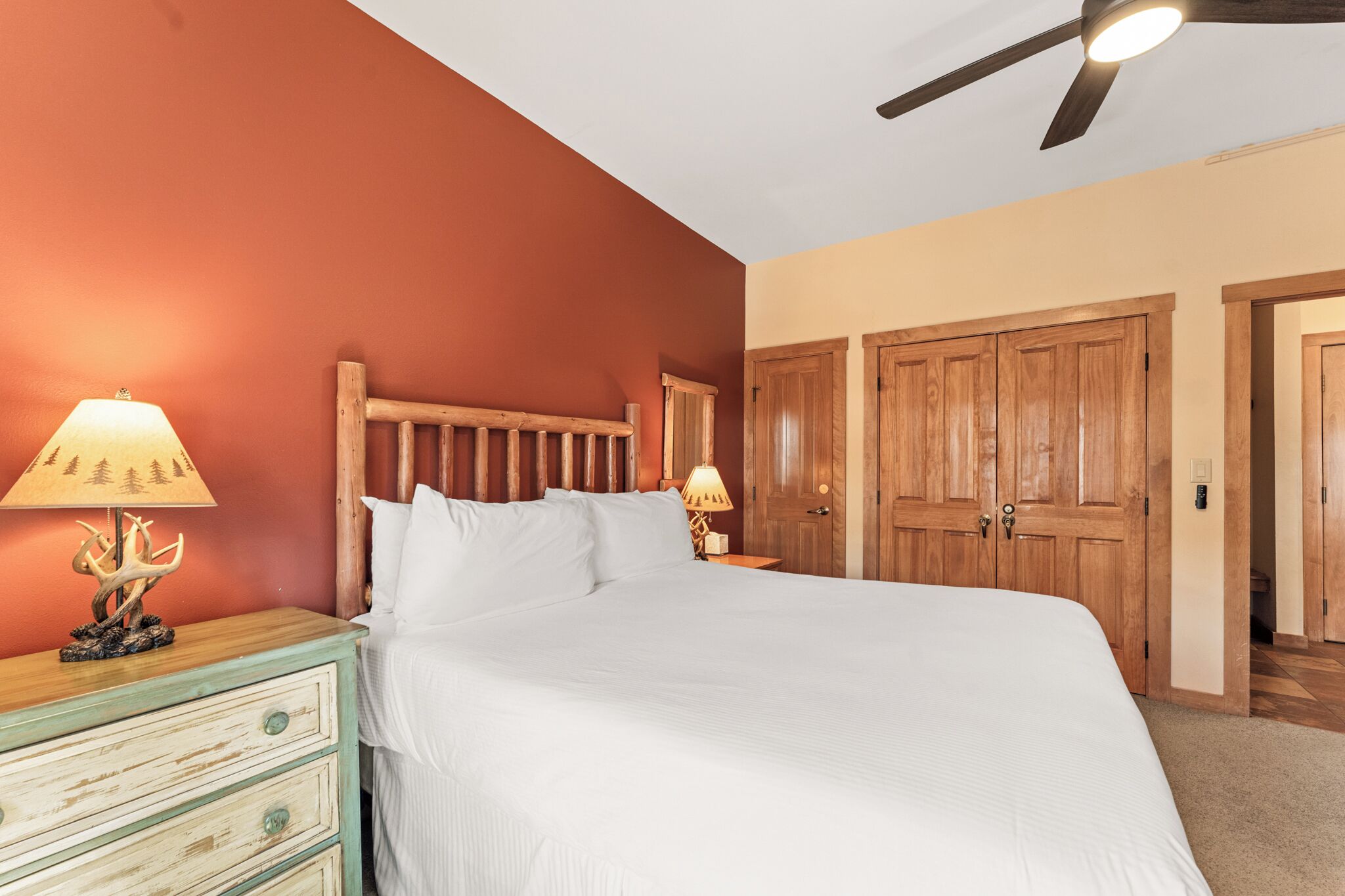 A bedroom with a large bed, wooden headboard, two bedside lamps, and a ceiling fan.