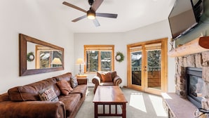 A living room with a brown leather sofa, a wooden coffee table, a fireplace, and a ceiling fan.