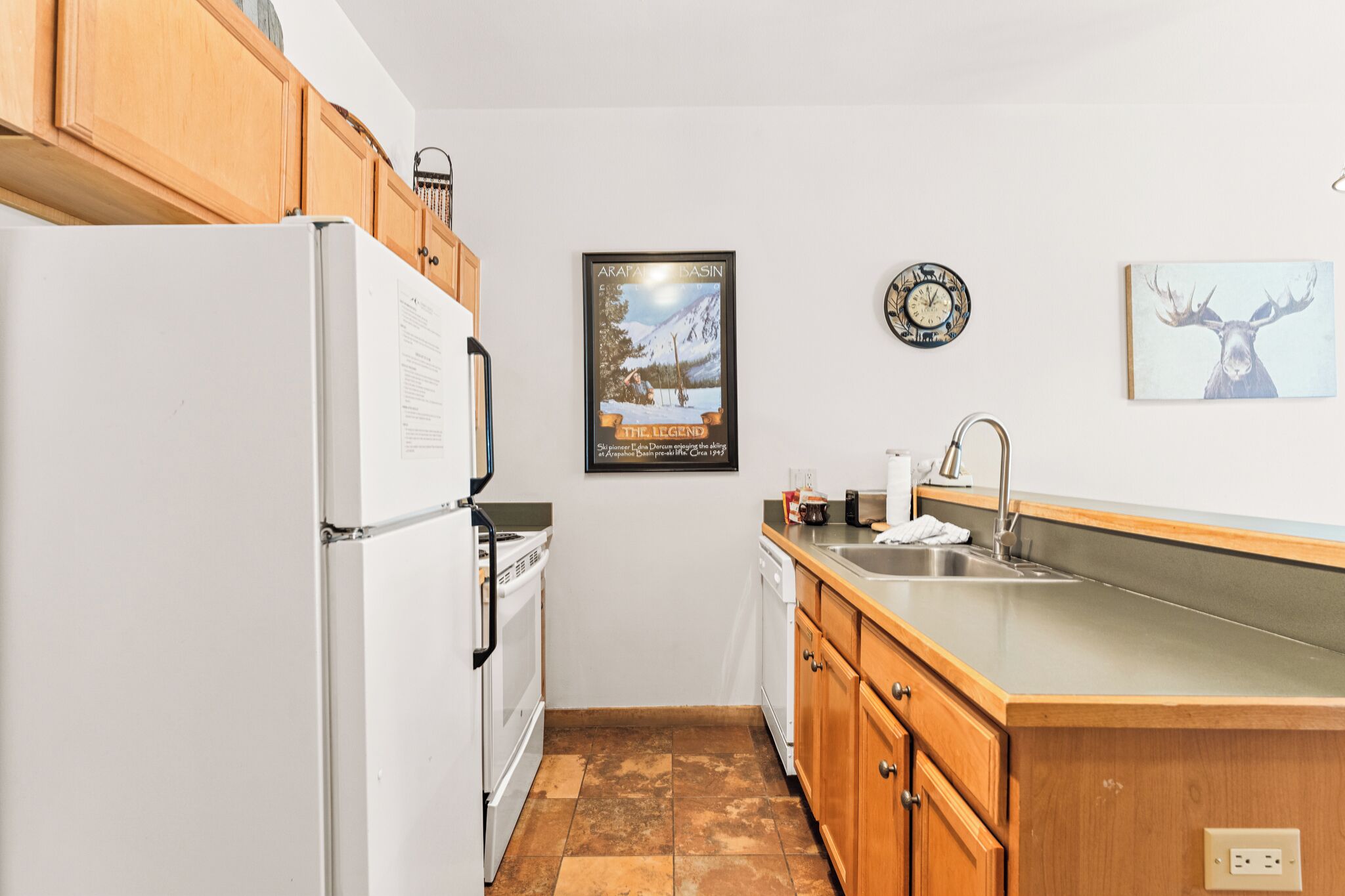 A kitchen with wooden cabinets, a white refrigerator, a stove, a dishwasher, a sink, and a clock on the wall.