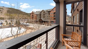 A balcony with a wooden bench, overlooking a parking lot and a building complex with multiple floors and a mix of brick and wood exteriors. - Dl8497-2 (Keystone)