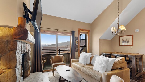 A cozy living room with a stone fireplace, a sofa, a coffee table, and a dining area with a wooden table and chairs. - Dakota Lodge #8538 (Keystone)