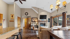 A spacious living area with a stone fireplace, a large TV mounted above it, and a wooden dining table. - Dakota Lodge #8538 (Keystone)