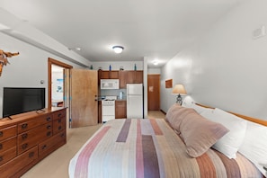 A compact hotel room with a bed, a TV, a wooden dresser, a kitchenette, and a bathroom. - Oro Grande #206 (Keystone)