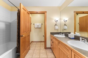 A bathroom with a bathtub, two sinks, wooden cabinets, a mirror, and a shower curtain. - Dl8520-2 (Keystone)