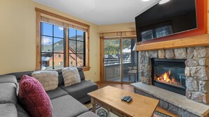 A living room with a stone fireplace, a gray sofa, and a large window overlooking a mountain. - Dl8520-2 (Keystone)