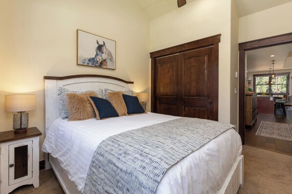 Une chambre à coucher avec un grand lit, une armoire en bois, une table de chevet avec une lampe et un tableau encadré au mur.