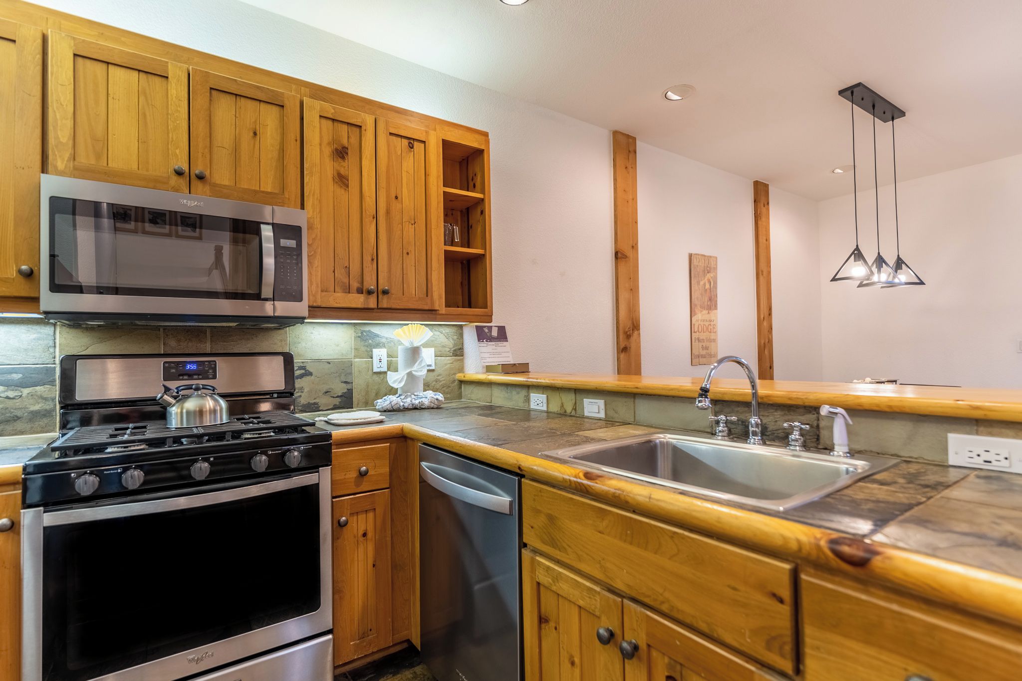A kitchen with wooden cabinets, a stainless steel microwave, a gas stove, and a sink.