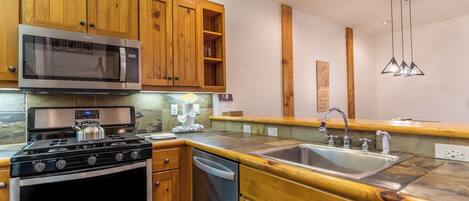A kitchen with wooden cabinets, a stainless steel microwave, a gas stove, and a sink.