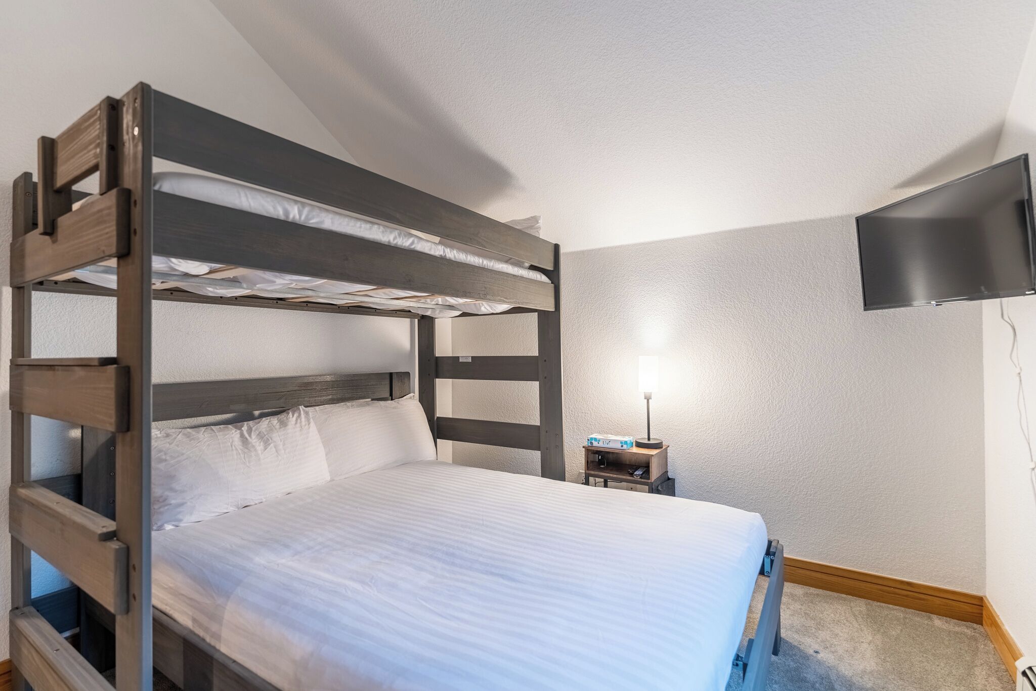 A bunk bed room with a flat-screen TV mounted on the wall.