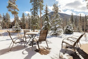 A wooden deck with metal chairs and a table, surrounded by snow-covered trees and a mountain in the background. - St8715-2 (Keystone)