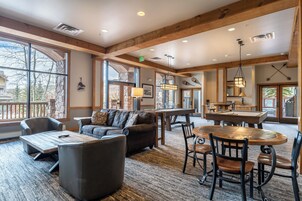 A spacious living area with a large wooden table, comfortable seating, and large windows offering views of the outdoors.
