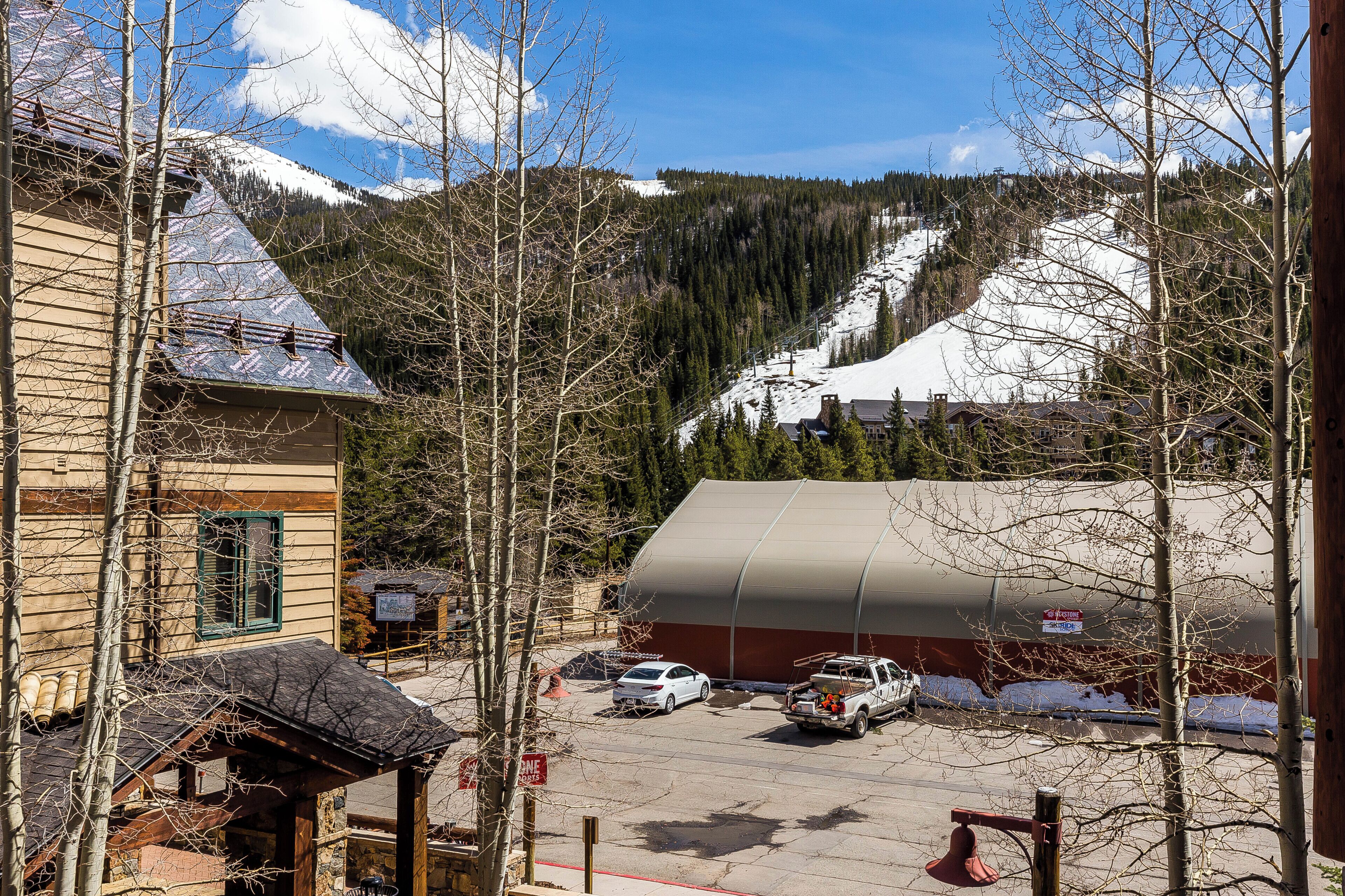 A mountain lodge with a parking area, snow-covered slopes, and a clear sky.