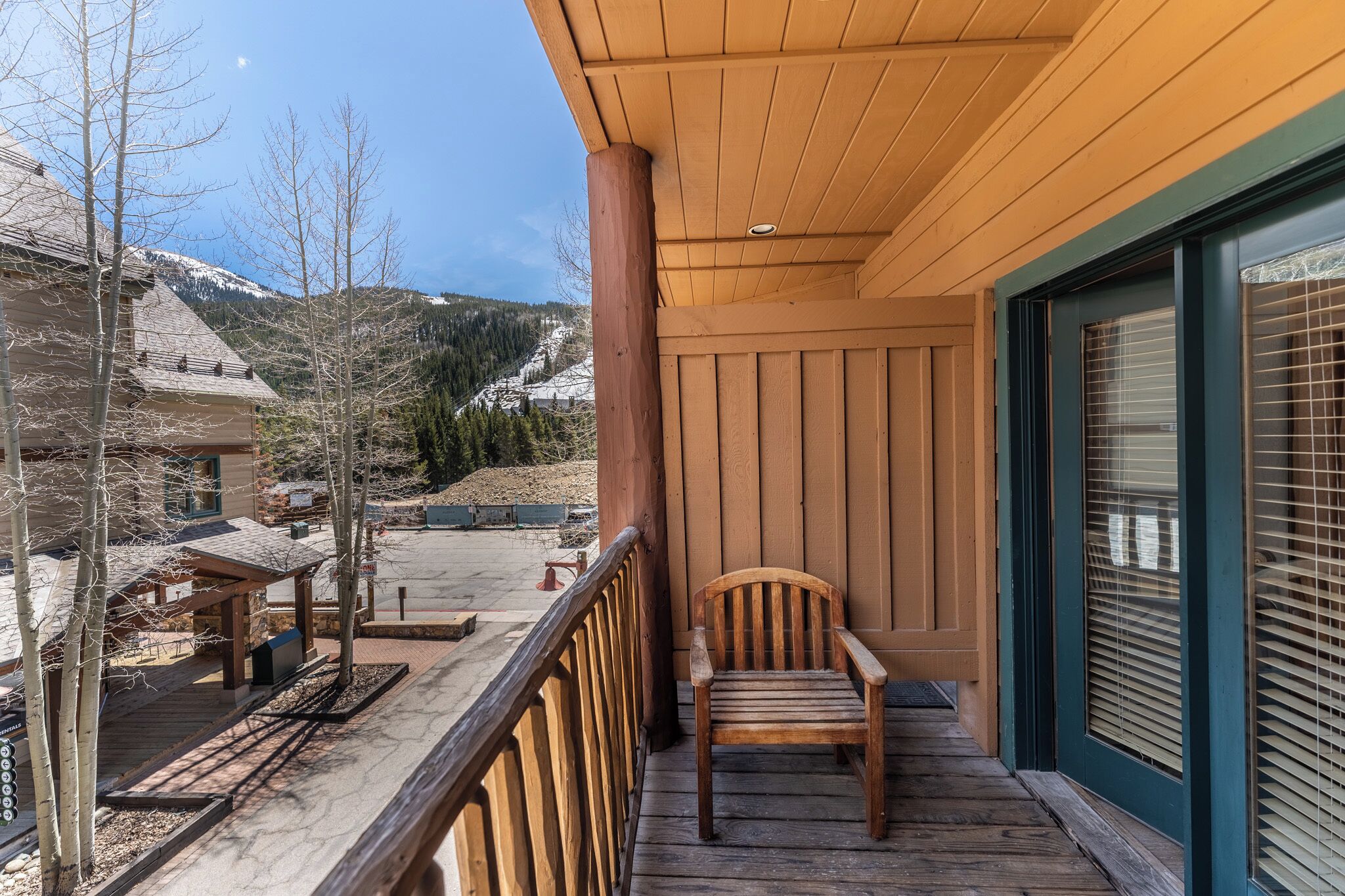 Una terraza de madera con una silla, un área techada y vistas a una montaña nevada.