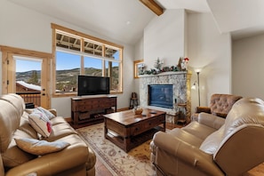 A spacious living room with a large window, a fireplace, leather sofas, and a television. - A39-3 (Keystone)