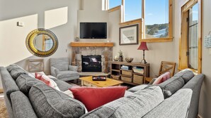 Een gezellige woonkamer met een open haard, comfortabele zithoeken en een groot raam met een prachtig uitzicht.