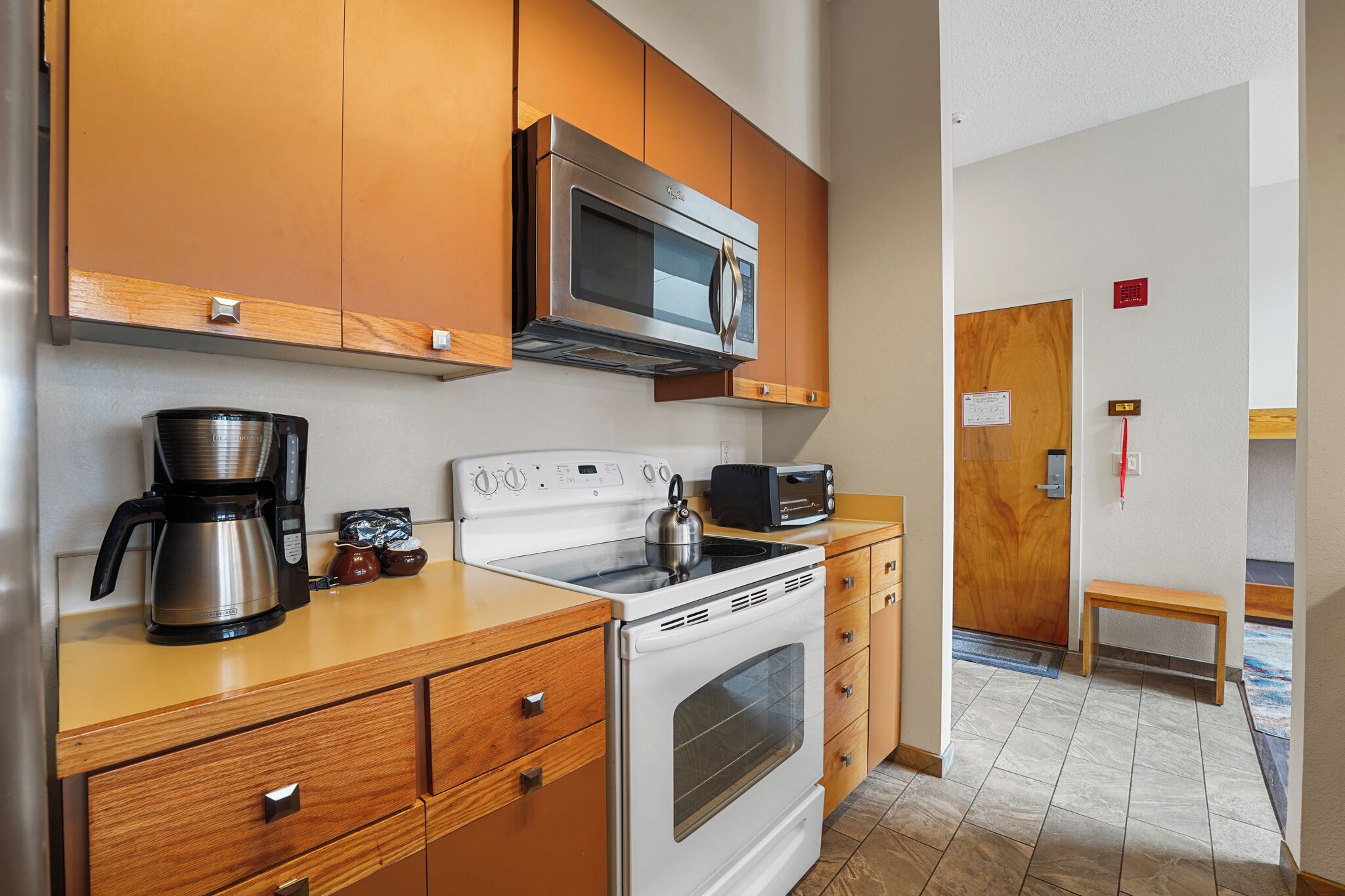 A compact kitchen with wooden cabinets, a microwave, a stove, a coffee maker, and a toaster.