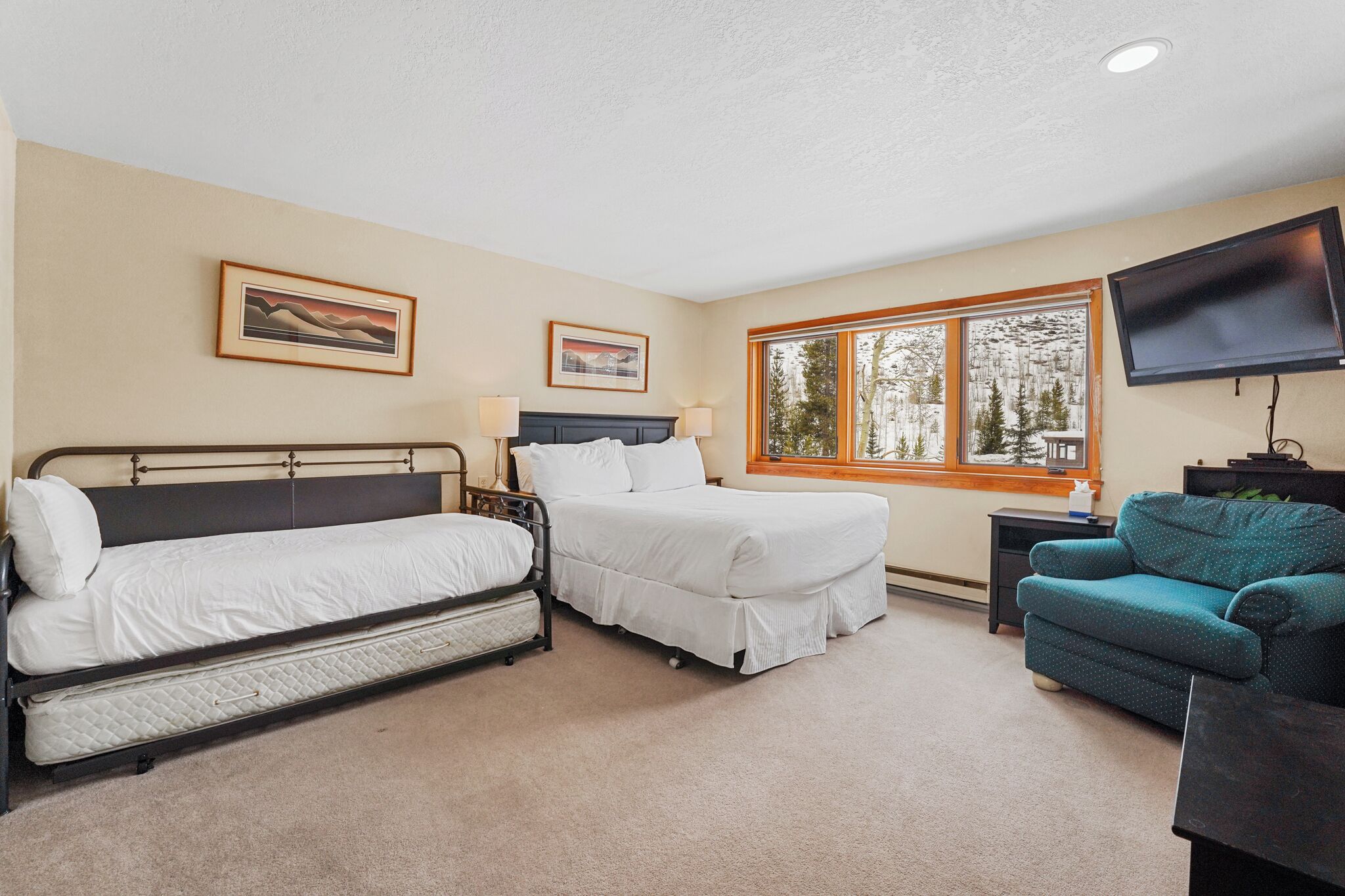 A hotel room with two beds, a TV, a window with a view of trees, and artwork on the walls.