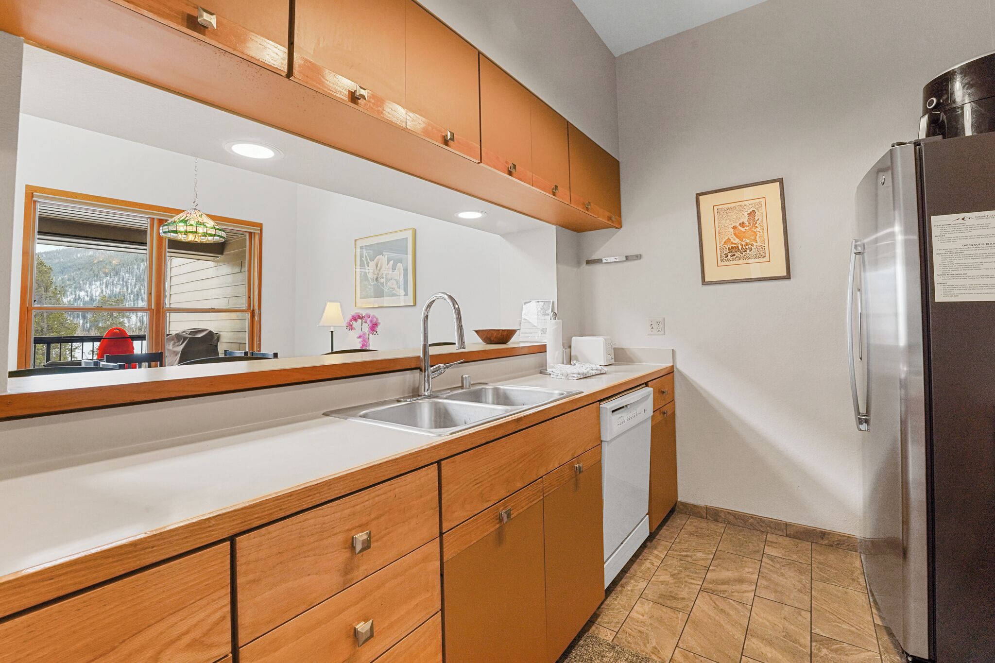 A modern kitchen with wooden cabinets, stainless steel appliances, and a large window.