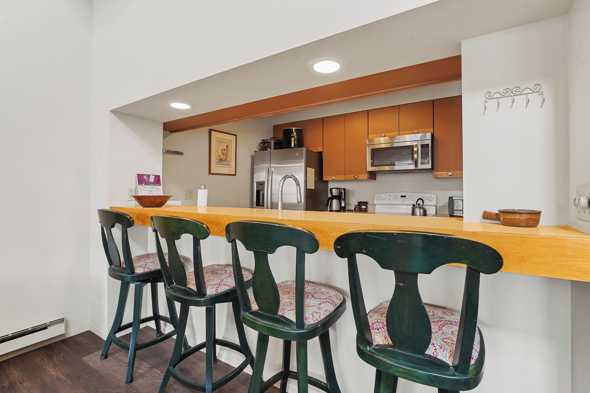A kitchen with wooden bar stools, a stainless steel refrigerator, and a microwave.