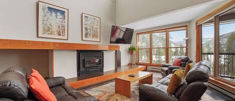 A spacious living room with a fireplace, leather sofas, a coffee table, and large windows offering a mountain view.