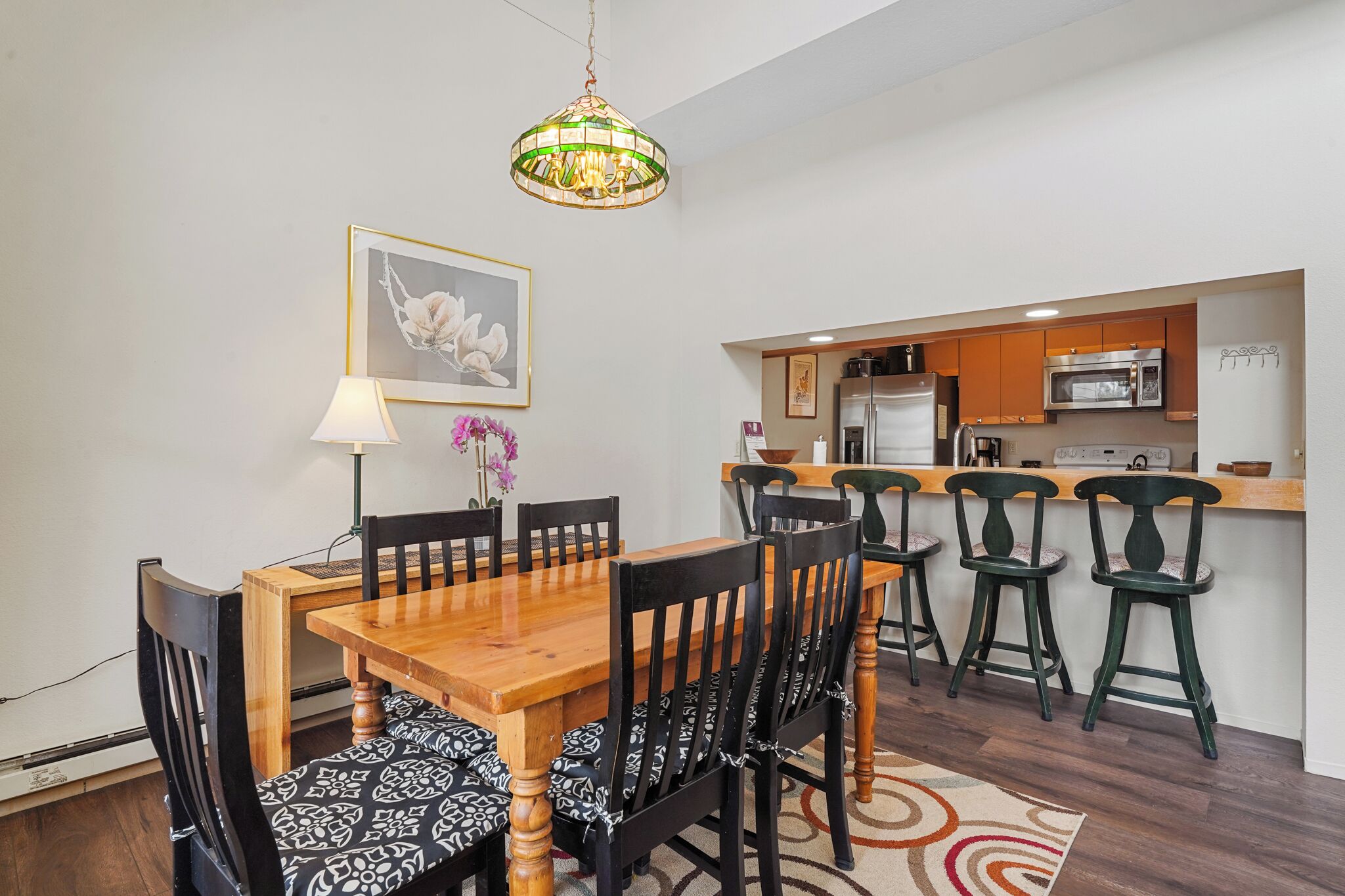 Un'area pranzo con un tavolo e sedie in legno, un lampadario e una cucina sullo sfondo.