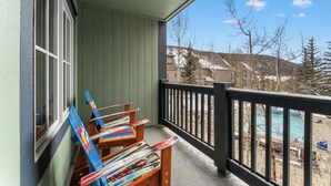 A balcony with skis leaning against the wall, a pool, and a view of buildings and trees. - Expedition Station #8582 (Keystone)