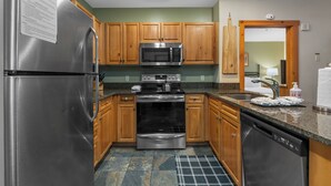 A kitchen with stainless steel appliances, wooden cabinets, granite countertops, and a tiled floor. - Expedition Station #8582 (Keystone)