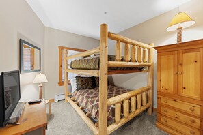 A bunk bed with a wooden frame, a television on a desk, a lamp, and a wooden dresser. - Expedition Station #8553 (Keystone)