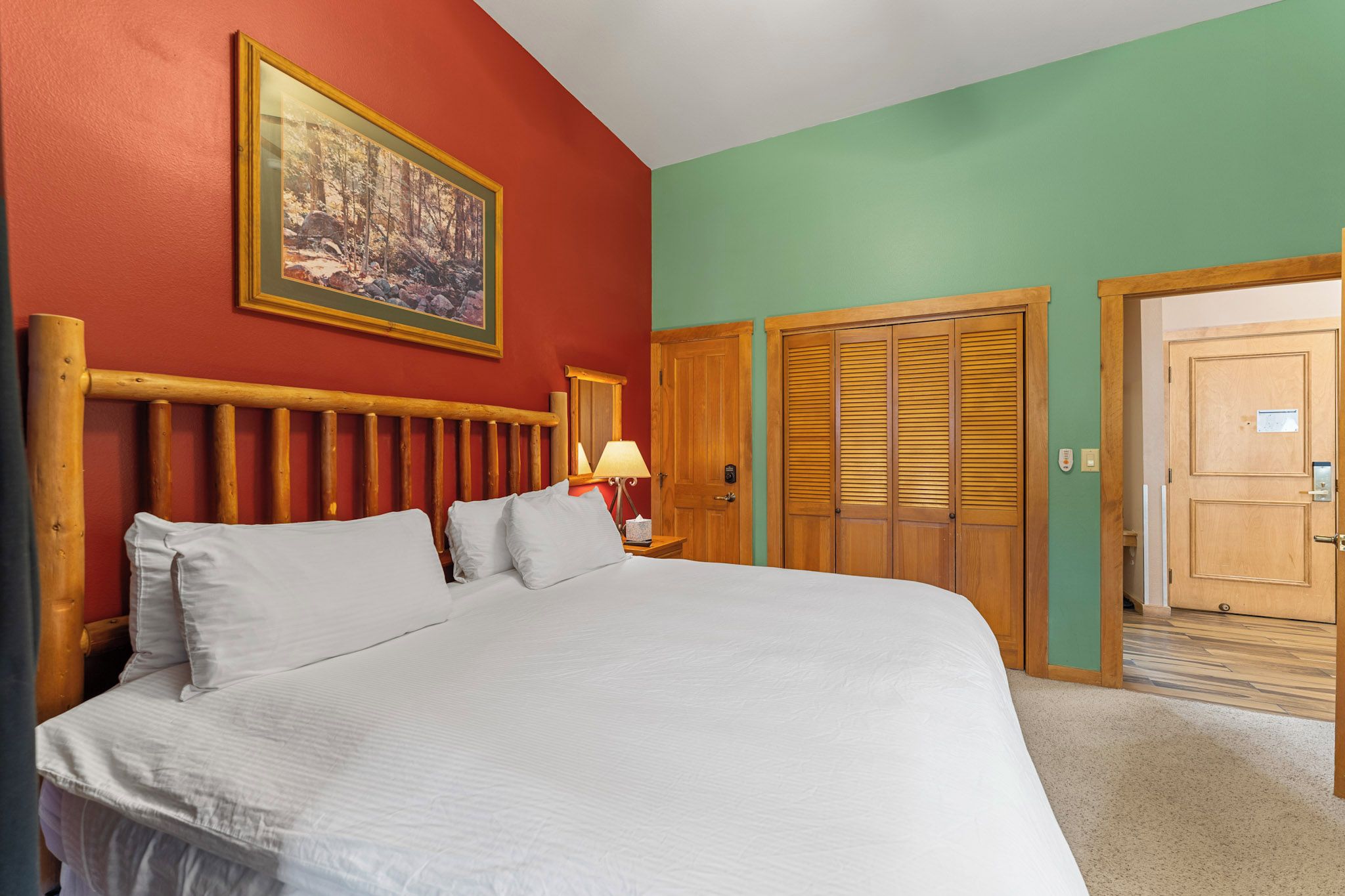 A room with a large bed, a wooden headboard, a painting on the wall, and a door with a wooden frame.