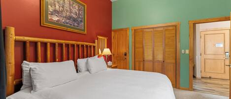 A room with a large bed, a wooden headboard, a painting on the wall, and a door with a wooden frame.