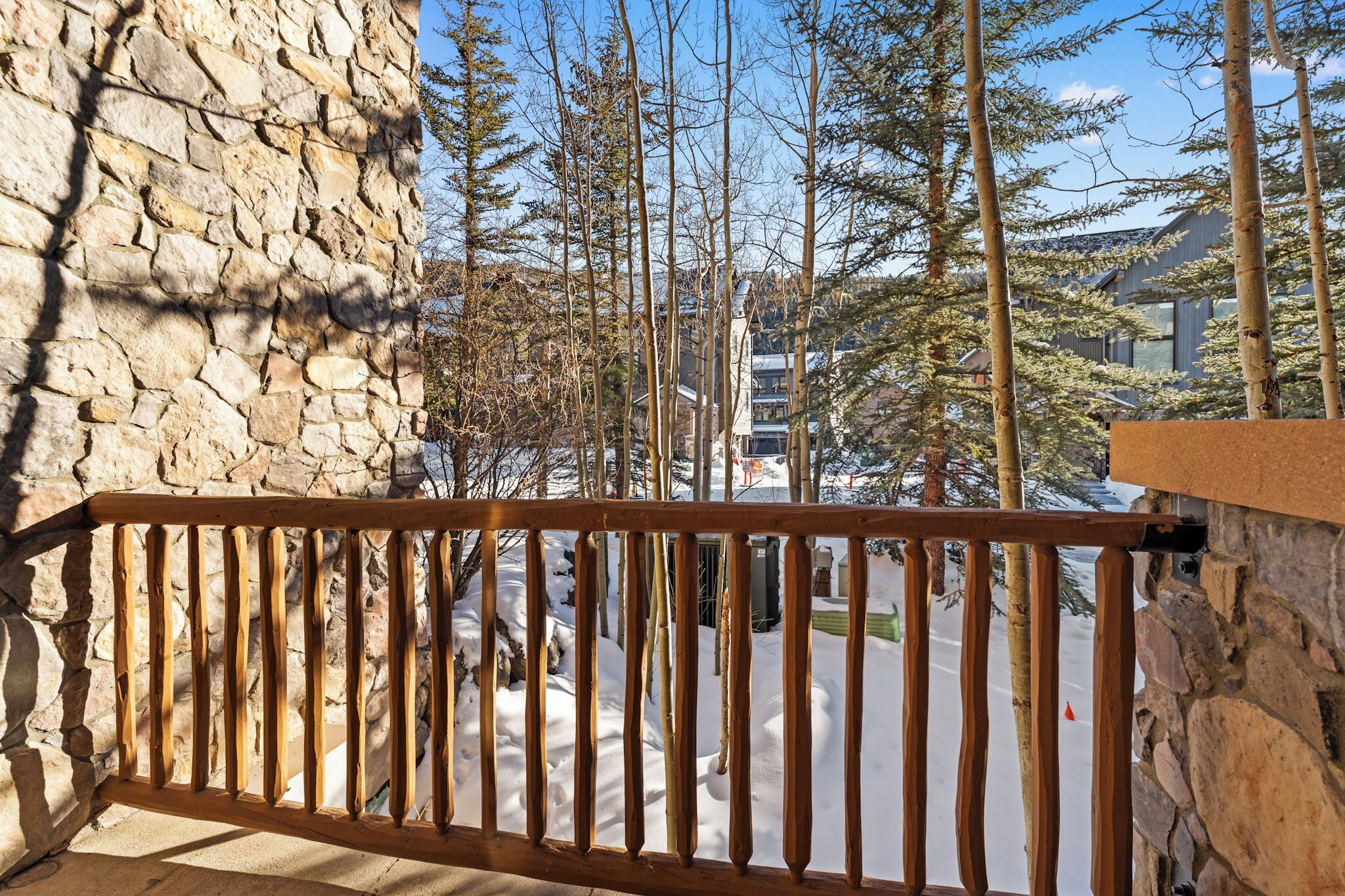 A stone wall and wooden railing overlooking a snowy landscape with trees and a modern building in the background.