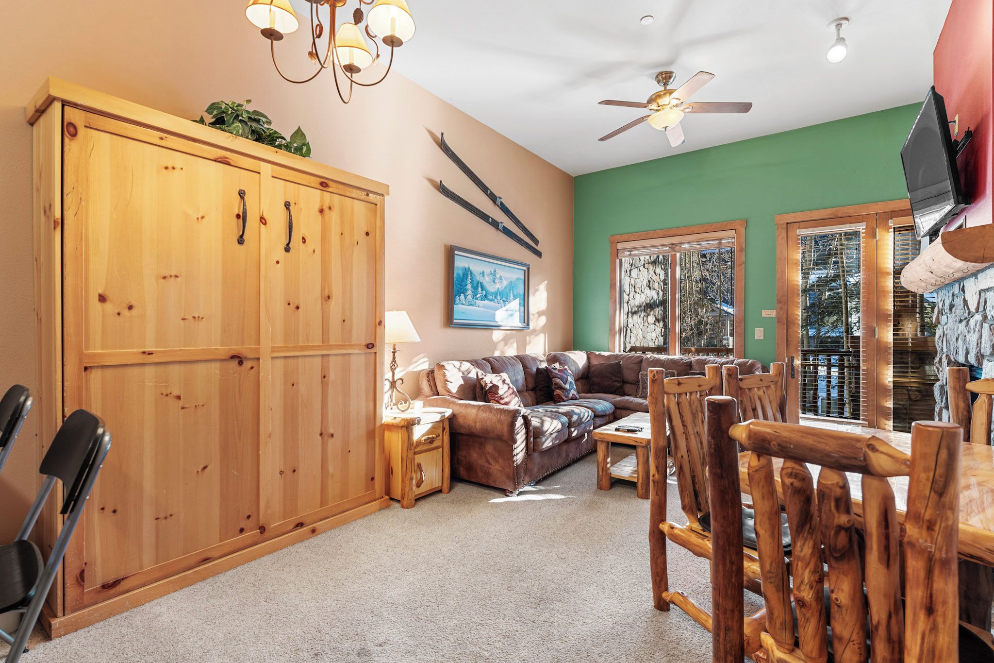 A cozy living room with a wooden cabinet, a leather sofa, a dining table with wooden chairs, and a ceiling fan.