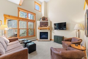 A cozy living room with a fireplace, comfortable seating, and large windows offering a view of the outdoors. - Trapper's Crossing #8772 : 2 (Keystone)
