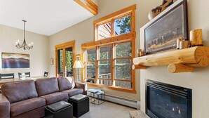 Una sala de estar acogedora con chimenea, ventanas grandes, un sofá y un comedor.