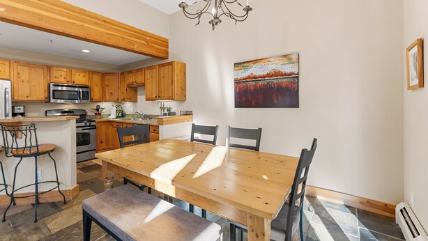 Una cocina moderna con armarios de madera, un microondas de acero inoxidable y un comedor con mesa y sillas de madera.