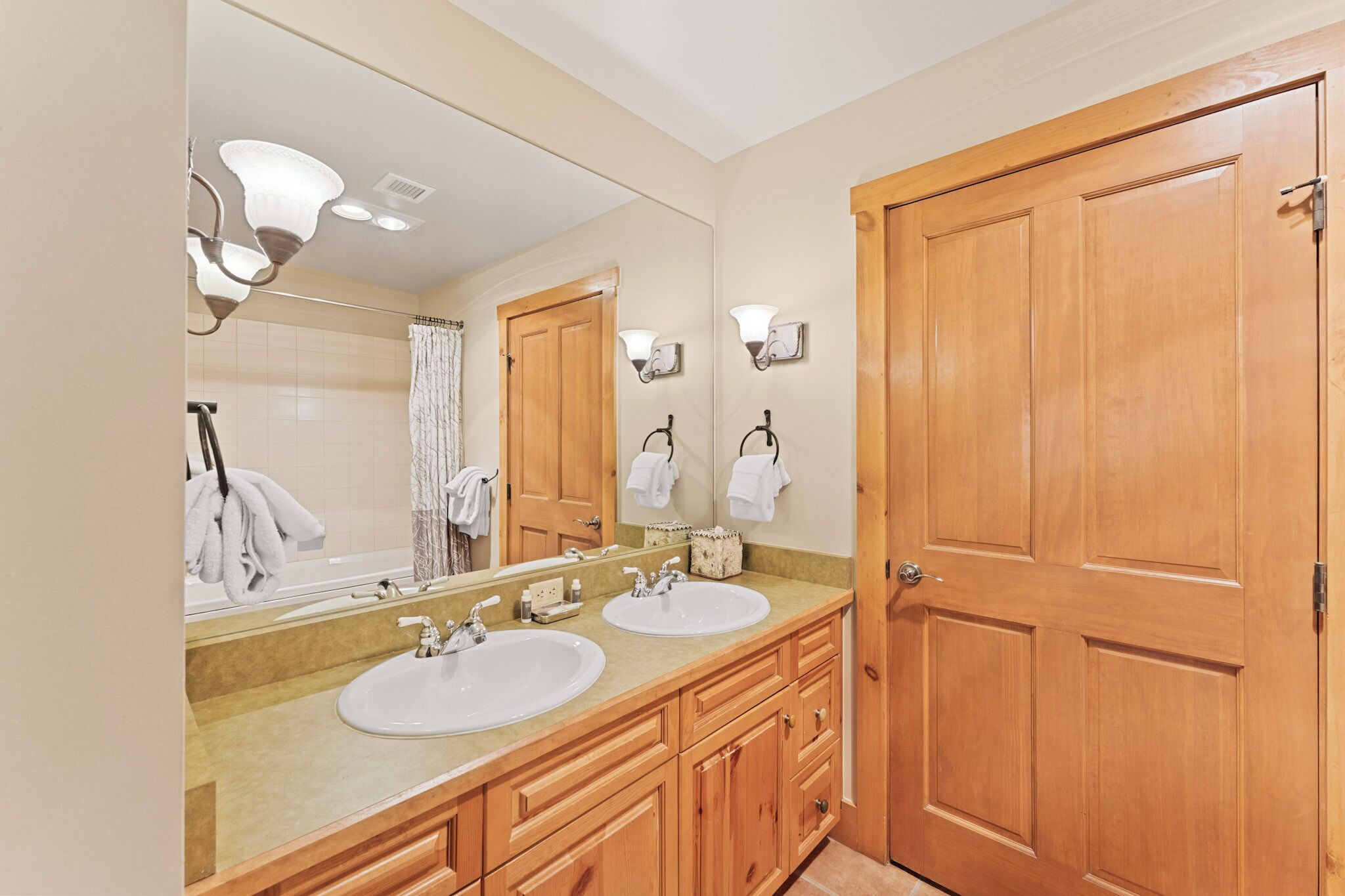 A bathroom with two sinks, wooden cabinets, a large mirror, and a wooden door.