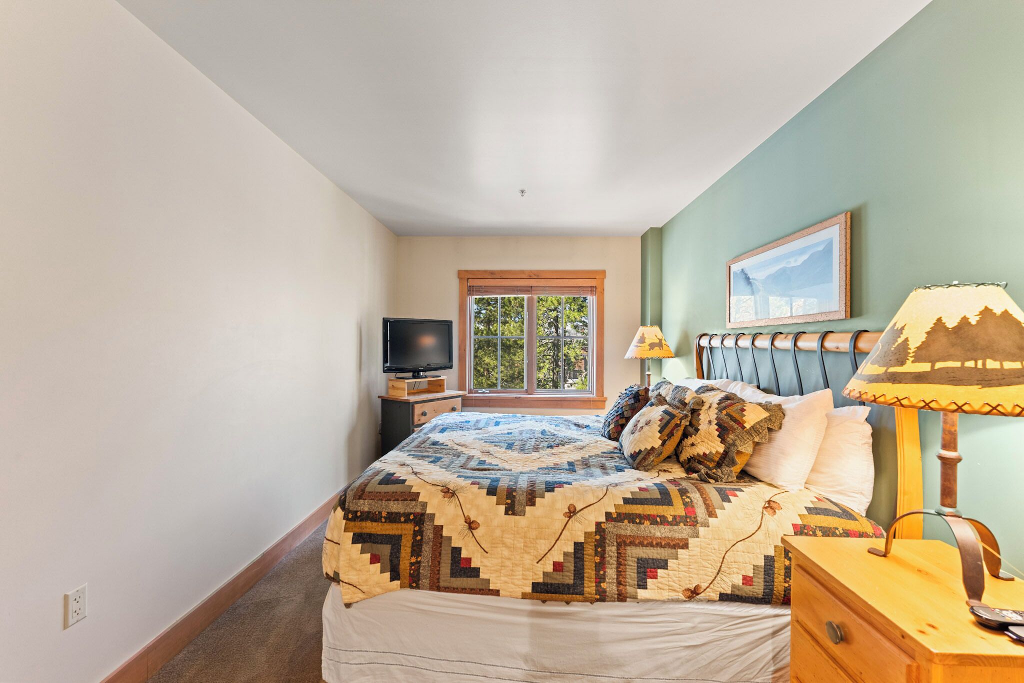 Un dormitorio con cama, mesita de noche, lámpara, televisor y ventana.